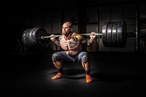 Bodybuilder squatting a heavy barbell in a dark gym