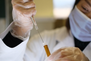 Gloved hands drawing liquid from a vial with a syringe